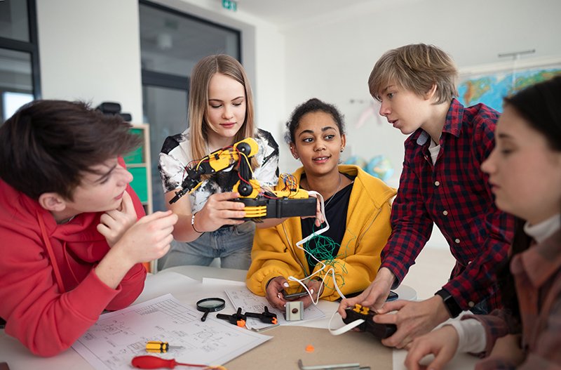 Group of students building and programming electric toys and robots at robotics classroom